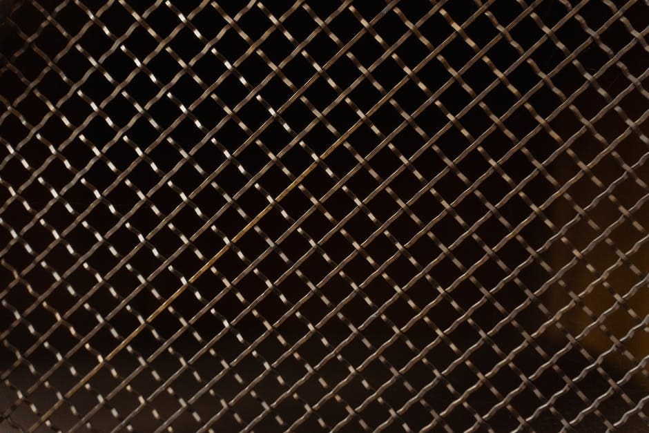 A close-up photograph of a chain link fence with a warm, dark brown metallic finish and consistent diagonal diamond pattern.