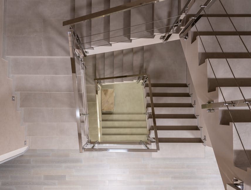 An overhead view of a modern staircase with metal handrails and light-colored steps, photographed from above looking down.