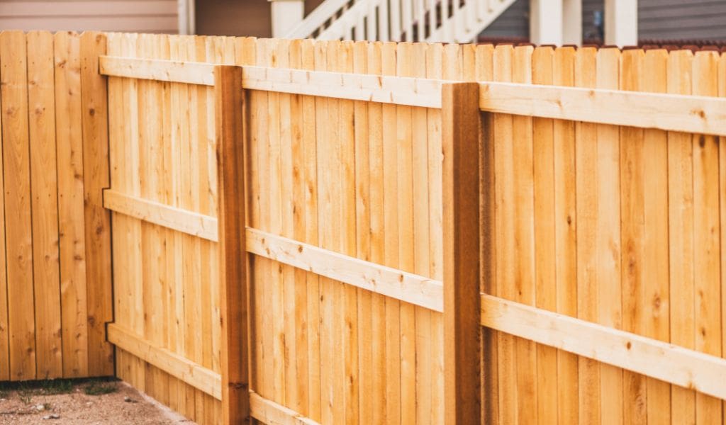 A newly constructed wooden fence with horizontal panels and white rails photographed in daylight at a residential property.